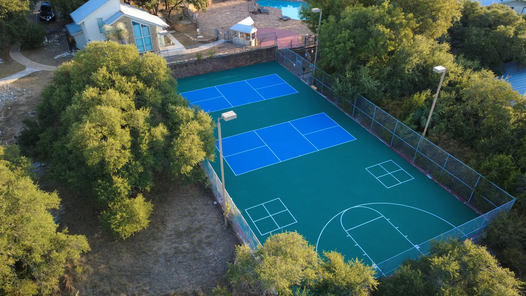 Two newly resurfaced lighted pickleball courts and basketball court at Baycliff Apartments, Horseshoe Bay TX — aerial view with Hill Country oaks