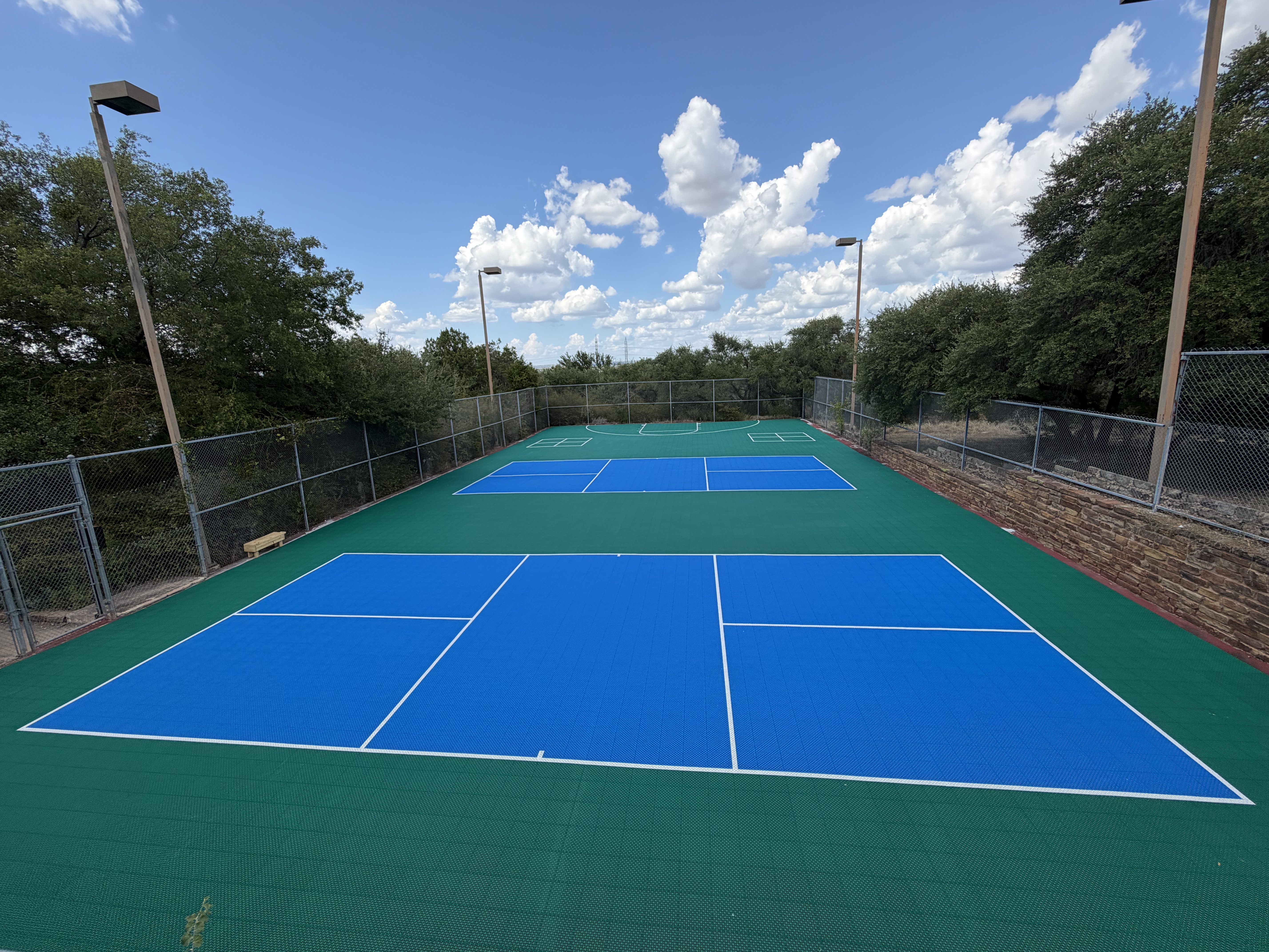 Center view of Baycliff Apartments pickleball and basketball courts with lighted poles and Hill Country oak trees