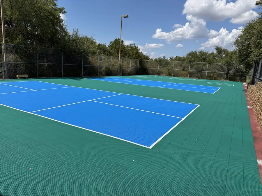 Sideline view of Baycliff Apartments pickleball courts with stone retaining wall and Texas Hill Country oaks
