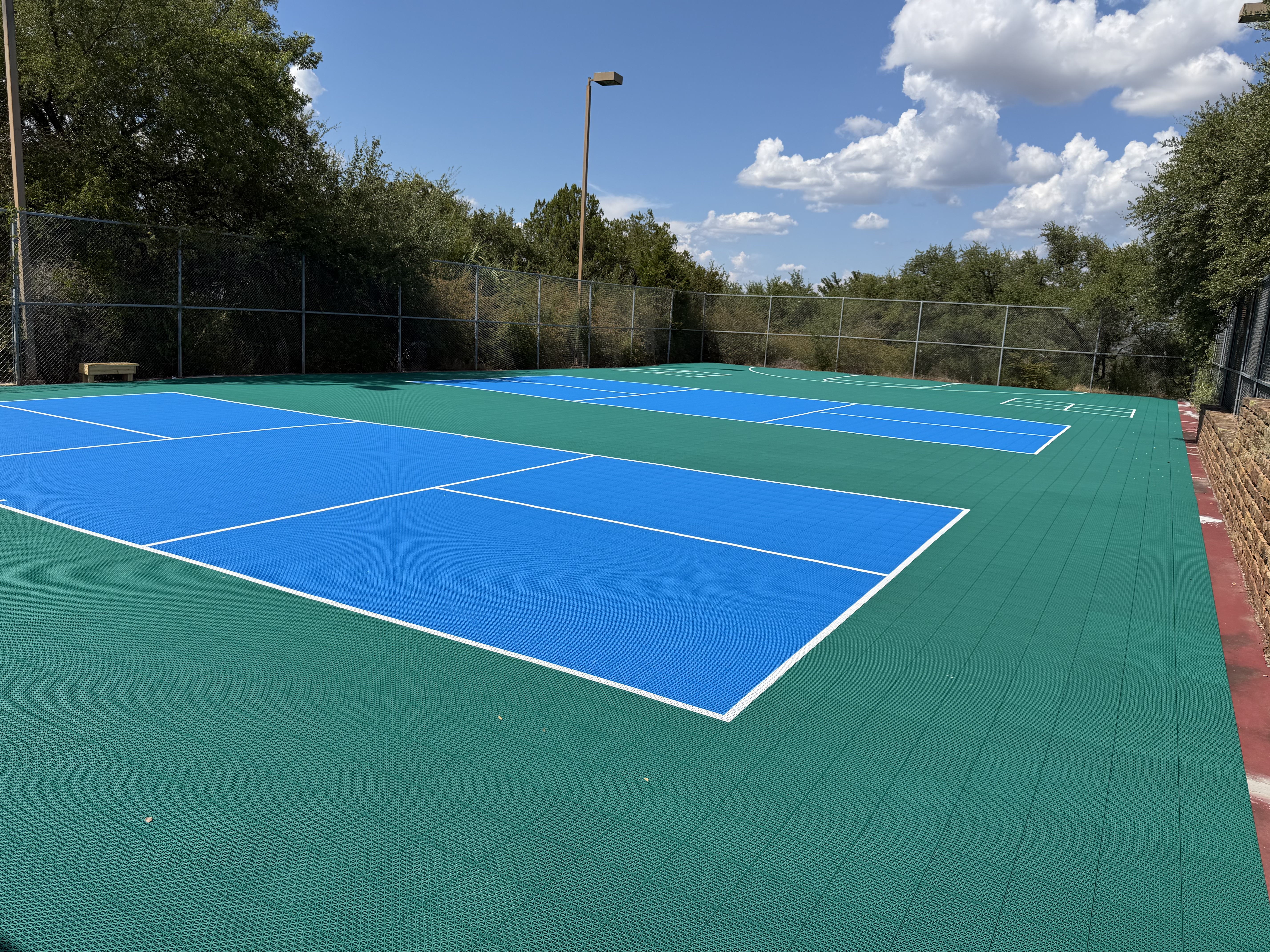 Sideline view of Baycliff Apartments pickleball courts with stone retaining wall and Texas Hill Country oaks